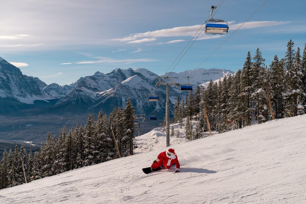 Snowboarder in a Santa costume riding down a run at Banff, with Rocky Mountain peaks in the background