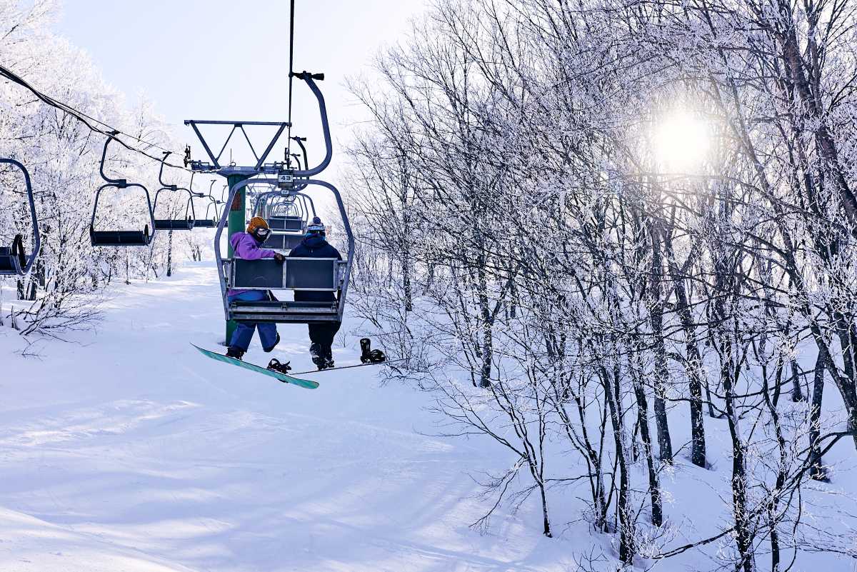 Snowboarder riding a chairlift through frosted trees at Madarao, Japan