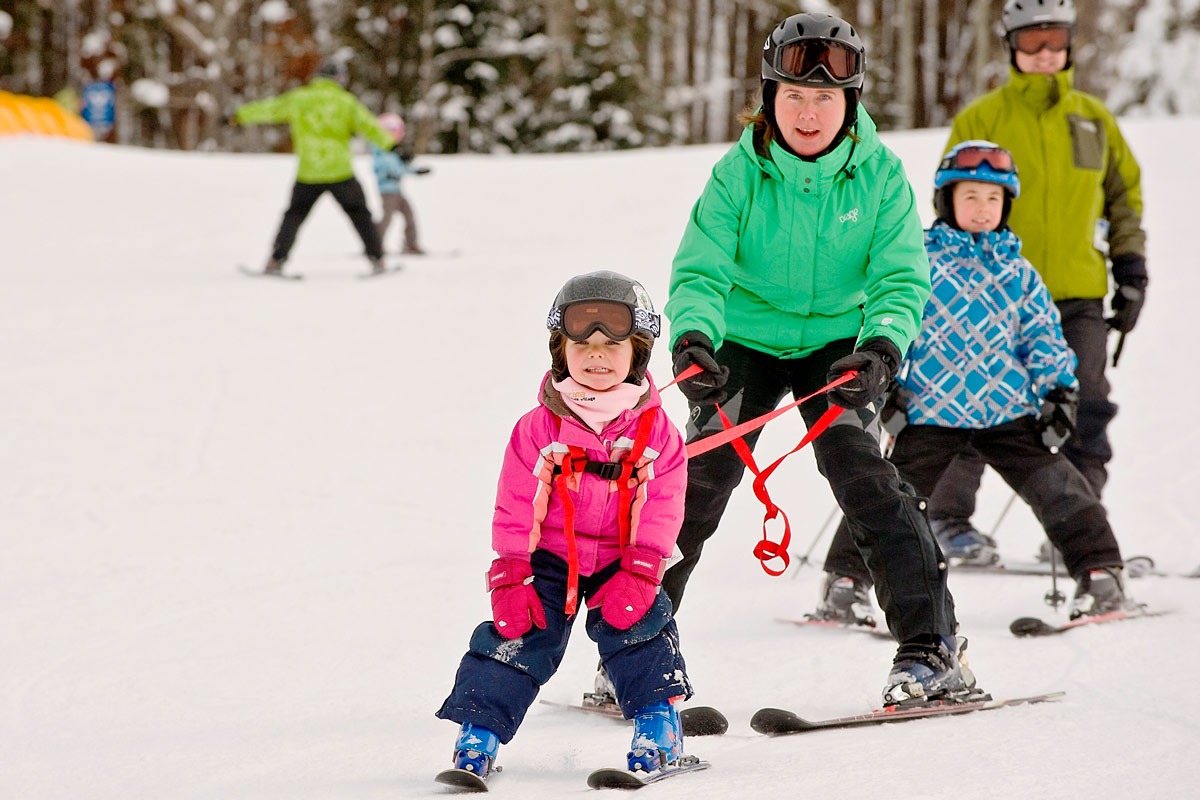 Young child learning to ski with a harness alongside an instructor at Panorama Mountain Resort
