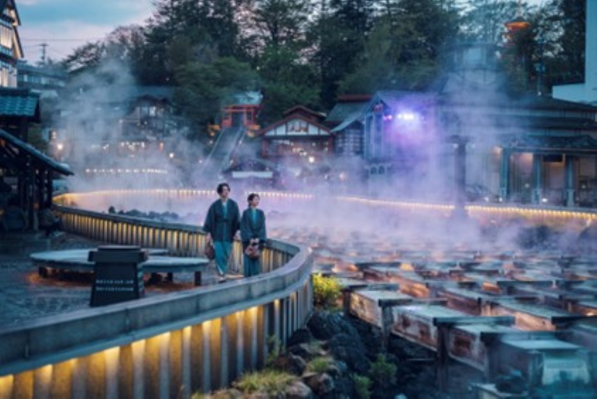 Guests in yukata walking beside the Yubatake hot spring field in Kusatsu Onsen at dusk
