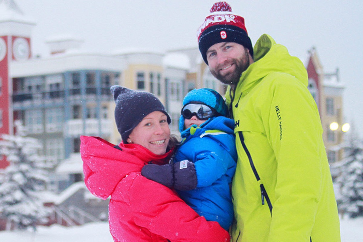Family in ski gear smiling together in front of SilverStar's village buildings"