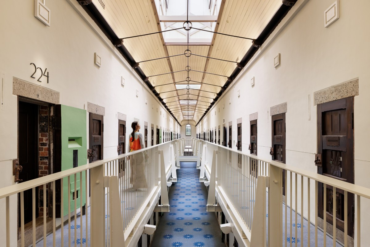 Guest walking along a preserved cell corridor at HOSHINOYA Nara Prison, original doors and numbering intact