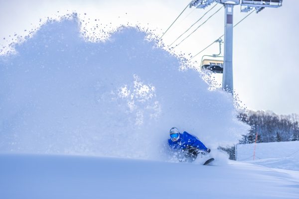 Snowboarder spraying powder beside a chairlift at Madarao, Japan