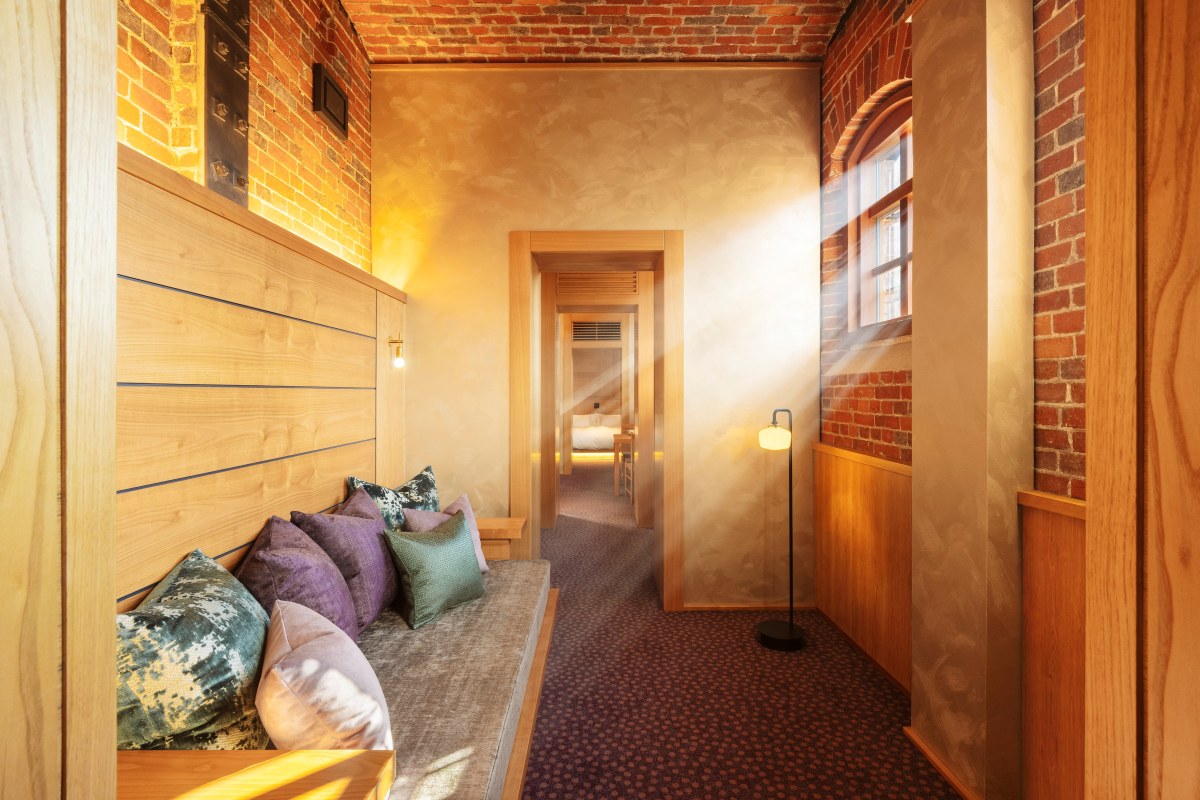 Suite corridor at HOSHINOYA Nara Prison with exposed brick, wooden bench seating and view through to the bedroom